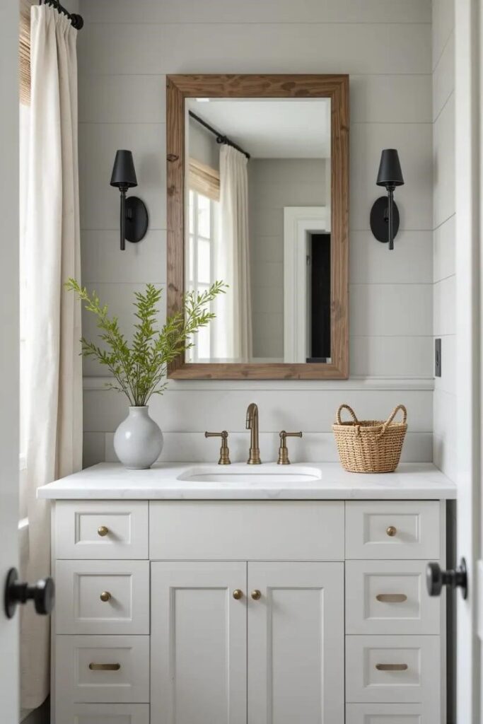 Soft gray shiplap accent wall in a modern farmhouse bathroom with brass fixtures and rustic wood decor.