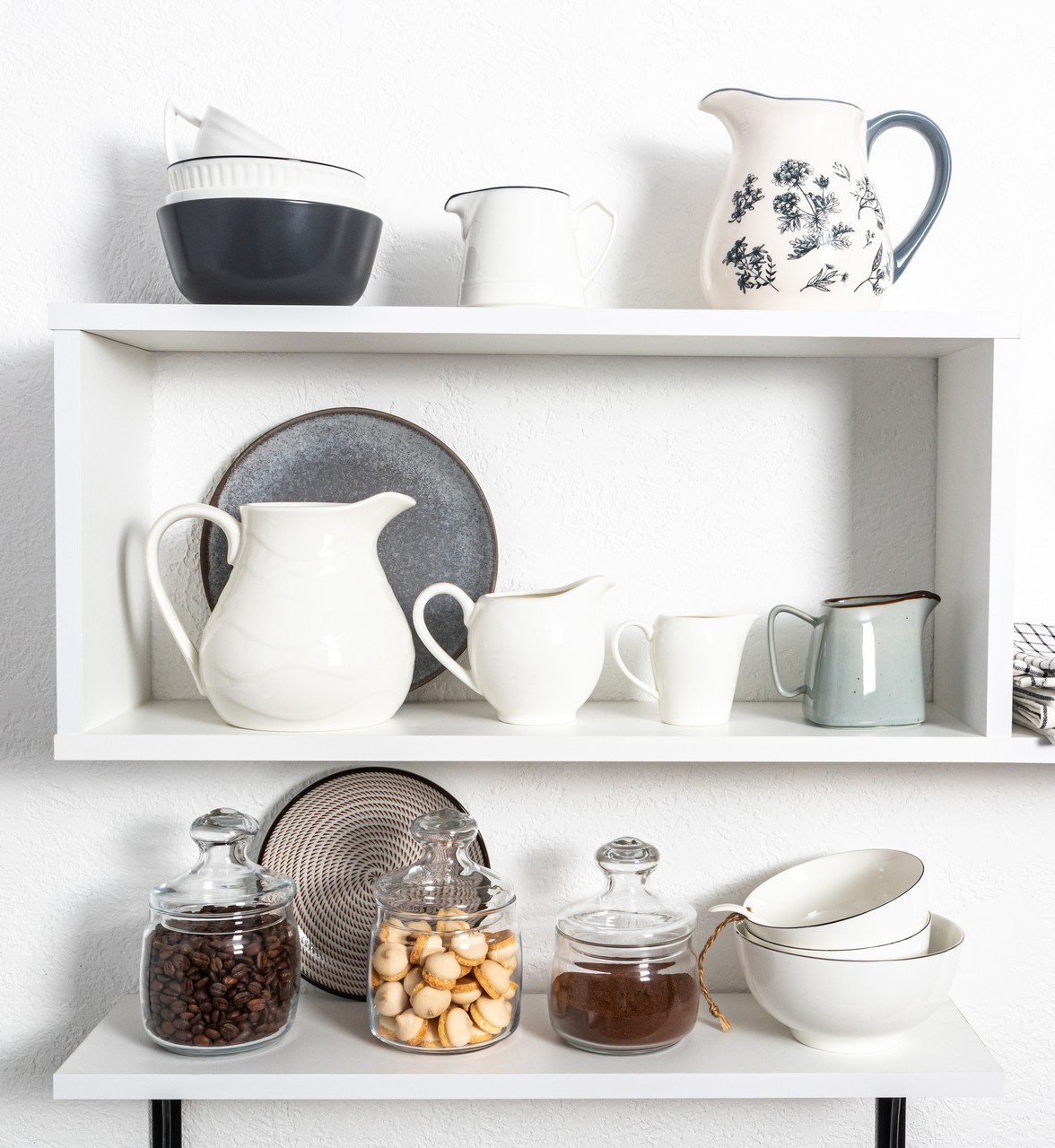 beautiful white shelves with kitchen utensils on a white textured wall. kitchen interior in white tones. front view. ecologically clean kitchen
