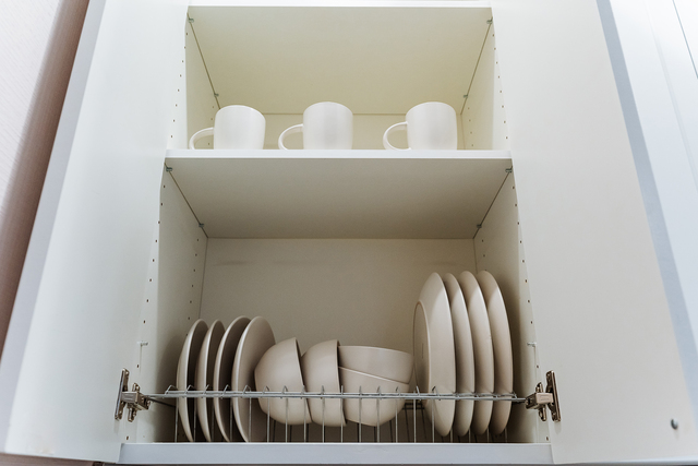 stacked plates and cups inside cabinet, soft natural light highlights smooth ceramic surfaces, wire rack holds organized dinnerware, neutral tones and clean lines convey minimalist aesthetic, home