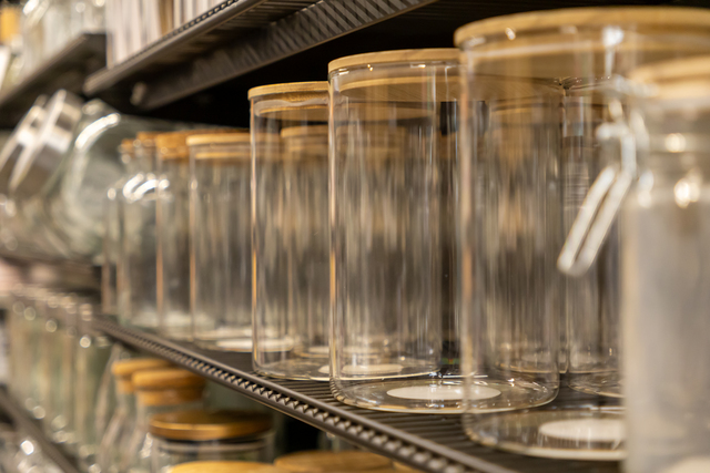 A close-up view of various clear glass jars featuring natural wooden lids displayed on a retail shelf, ideal for home kitchen organization and eco-friendly storage