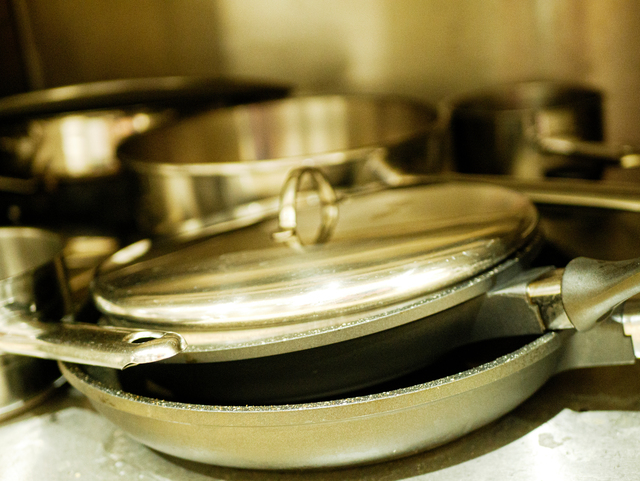 Close-up of stainless steel pans with lids stored on kitchen shelf in commercial restaurant workspace