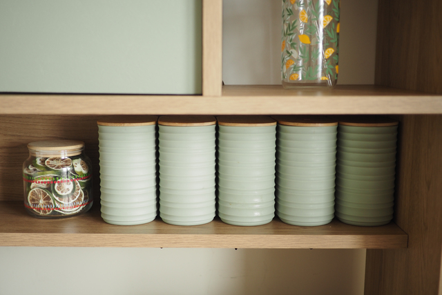 Green jars arranged on a wooden shelf in a kitchen