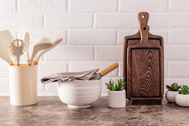 Kitchen utensils made of environmentally friendly materials on a modern marble countertop with indoor flowers. White brick wall.