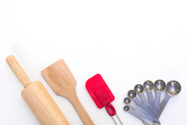 Top view kitchenware wooden rolling pin, wooden spatula, silicone spatula and steel measuring spoons on white background.