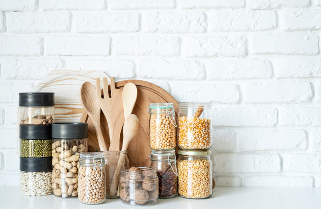 Various dried legumes in glass jars on white marble background
