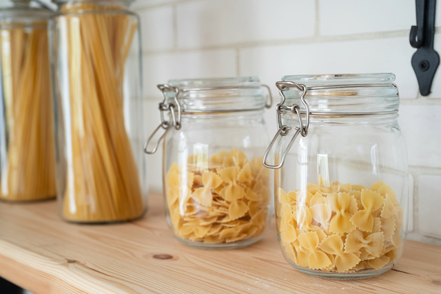 Wheat pasta in glass jar on a wooden shelf in the kitchen.