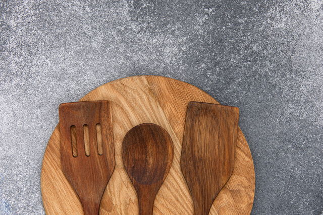 Wooden kitchen utensils arranged on a round wooden board on a gray surface